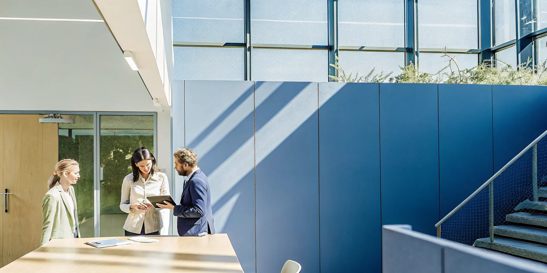 Three professionals reviewing a tablet in a sunlit modern office